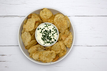 Snack food of potato crisps with sour cream and chive dip on white wood table.  With copy space. ...
