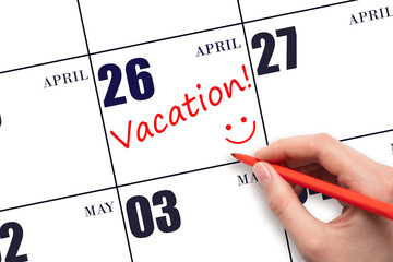 A hand writing a VACATION text and drawing a smiling face on a calendar date 26 April. Vacation...