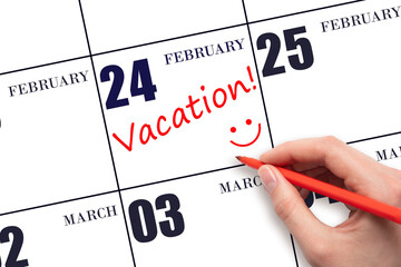 A hand writing a VACATION text and drawing a smiling face on a calendar date 24 February. Vacation...