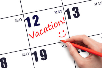 A hand writing a VACATION text and drawing a smiling face on a calendar date 12 May. Vacation...