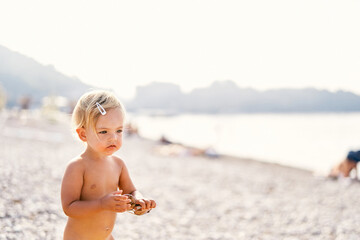 Little girl with sunglasses in her hands stands on the beach - Powered by Adobe