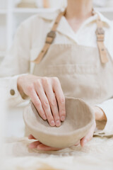 Obraz na płótnie Canvas woman ceramist in the workshop makes mugs out of clay. a small business or hobby is the creation of ceramic products. an oriental young woman ceramist makes dishes and vases out of clay. handmade