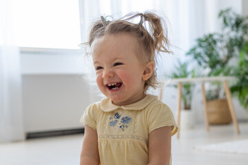 Cute caucasian preschool girl laughing out loud while sitting at home. Girl looking away with wide smile while having fun at apartments. Childhood concept. Stock photo - obrazy, fototapety, plakaty