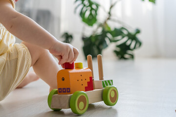 Cropped view of the baby girl playing at home alone with her children's coloured wooden toys for development. Kids playing with wooden train laying on the floor in her room