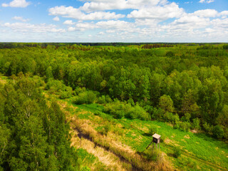 Fototapeta na wymiar Wide aerial view wooden hunting tower in sunny day. Aerial view from above big fields of farm land and one lonely wooden hunting tower