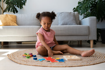 Black toddler playing with wooden blocks at home. Multiracial little girl is playing educational...