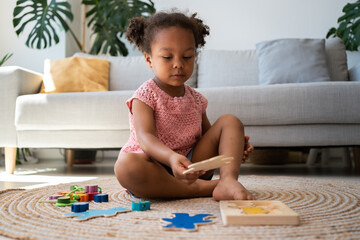 African american cute girl is playing educational logic games. Child with wooden puzzle toys....