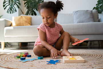 Multiracial cute girl play with eco-friendly toy puzzles on the floor in living room at home....