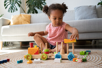 Child and play activities. Black kid girl play colourful wooden train in room. Baby building with...