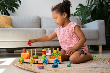 Educational eco-friendly toys. Afro two years old child girl playing with wooden colourful train at...