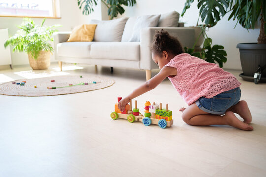 Little black attentive child girl playing wooden eco friendly railroad on the floor. Early learning and developing toys concept. Stock photo