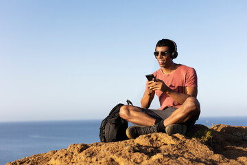 Young man sitting on the stone listening the music. Tourist man on the top of the mountain...