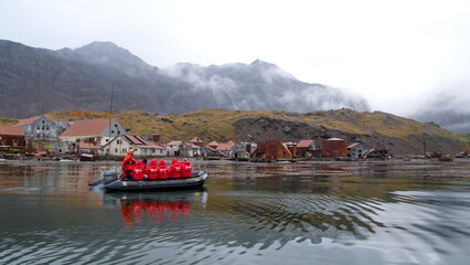 Zodiac inflatable boat from an expedition cruise ship at the rusted remains of a whaling station at Leith Harbor, South Georgia Island, under overcast skies