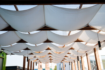 Patio made of white fabric on the roof, the design of an outdoor restaurant in the open air, the protection of cafe visitors in the summer heat, a place to relax in the shade.