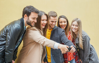 Young people using smartphones - Group of social media co workers having fun and takeing a selfie - Obsessed with online and shareing lifestyle moments -  Technology concept