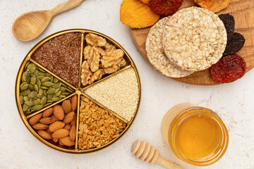 A round plate with nuts and seeds, honey, bread stand on a table with a light background. Concept: proper nutrition, breakfast, healthy food.