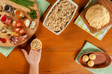 Woman hands preparing brazilian croquette (coxinha de frango) on a wooden kitchen table - Top view