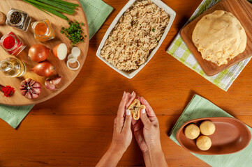 Woman hands preparing brazilian croquette (coxinha de frango) on a wooden kitchen table - Top view