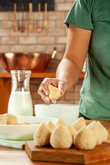 Woman hands breading brazilian croquette (coxinha de frango) with breadcrumbs on a wooden kitchen table.