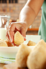 Woman hands breading brazilian croquette (coxinha de frango) with breadcrumbs on a wooden kitchen table.