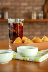 Fried brazilian croquettes (coxinha de frango) with iced soda in a kitchen with bricks wall.