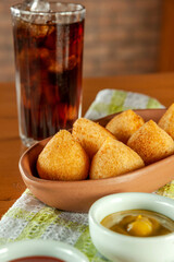 Fried brazilian croquettes (coxinha de frango) with iced soda in a kitchen with bricks wall.