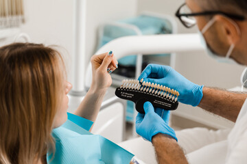 Woman looking at veneers or implants teeth color matching samples in doctor hands. Dentistry....