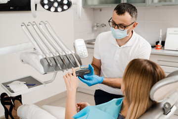 Dentist demonstrate teeth color shades guide for tooth whitening for woman patient in dental clinic. Dentistry. Woman looking at veneers or implants teeth color matching samples in doctor hands.