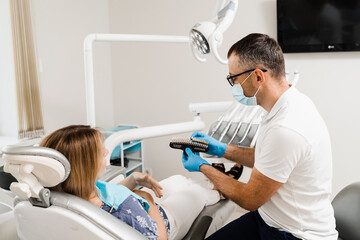 Dentist demonstrate teeth color shades guide for tooth whitening for woman patient in dental clinic. Dentistry. Woman looking at veneers or implants teeth color matching samples in doctor hands.