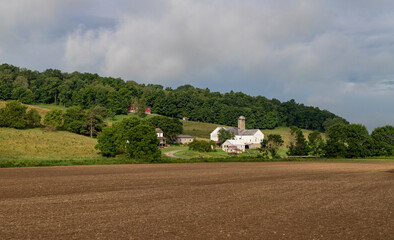 Amish farm on a wooded hillside with a newly planted dirt field in the foreground