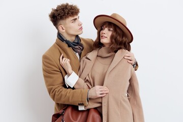 a sweet, joyful, pleasant stylish couple stands on a white background in autumn coats and gently hug each other, a man holds a woman by the coat looking at her