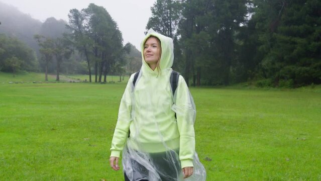 Cinematic portrait of young woman looking up at rain in nature. Traveler taking off raincoat hood making rain wet her blonde hair. Hiker girl on Hawaii Kokee park, Slow Motion RED camera. USA travel
