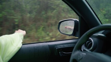 Cinematic inspirational video of young woman traveling by car or camper van with opened window to breathe fresh air of green rainforest, moves hand in rain.Summertime vacation vibes shot on RED camera