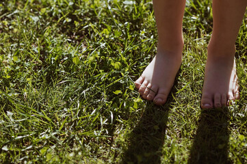 Close-up of a barefoot child walking on a grassy lawn in a park. The concept of a healthy lifestyle, freedom and outdoor recreation.