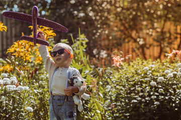A little boy in sunglasses launches a toy airplane in nature. Summer time, happy childhood, dreams...
