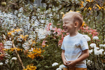 Cute happy boy playing with soap bubbles on a sunny summer day. A child in the fresh air, in nature. The concept of a happy childhood and a holiday.