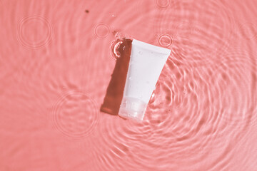 Obraz premium White cosmetic tube on the pink water surface. Blank label for branding mockup. Flat lay, top view. beauty spa medical skincare and cosmetic lotion bottle cream packaging product on pink background.
