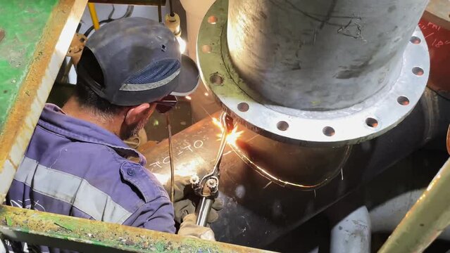 Repair of a marine vessel, a welder in protective glasses does welding of a larger pipe, a technological process.