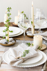 Rustic zero waste wedding decor with natural elements. Wooden table, candles, linen napkins, branches with green leaves. Eco-friendly decoration for the special dinner. Romantic and cozy place