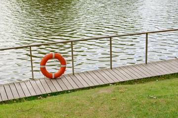 Orange lifebuoy near the pond. Saving and preserving human life. Safety on the water.