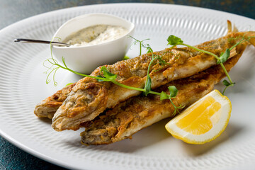 fried smelt on white plate with tar tar sauce and lemon macro close up