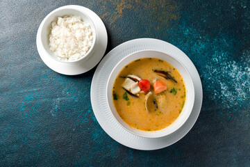 Tom Yam soup with seafood and boiled rice, hot and spicy soup on dark blue table top view