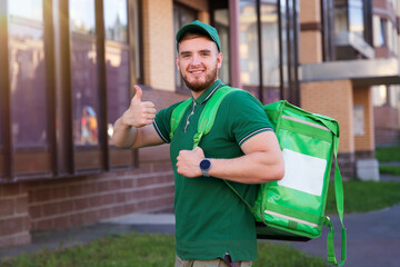 portrait of young handsome happy smiling courier guy, food delivery man with green thermo box for...