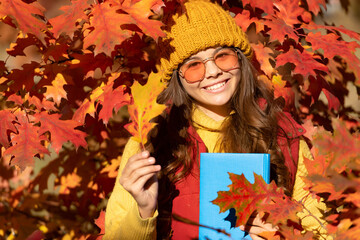 Naklejka na ściany i meble Autumn teen child girl portrait, fall leaves concept. cheerful kid hold book on autumn leaves background
