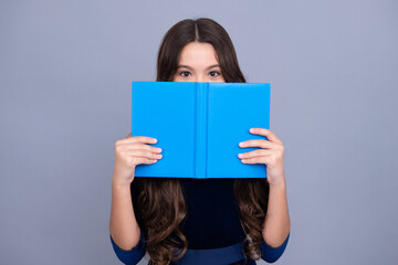 Obraz premium Schoolchild, teenage student girl hold book near eyes on gray isolated studio background. School and education concept. Back to school. Face hidden with book.