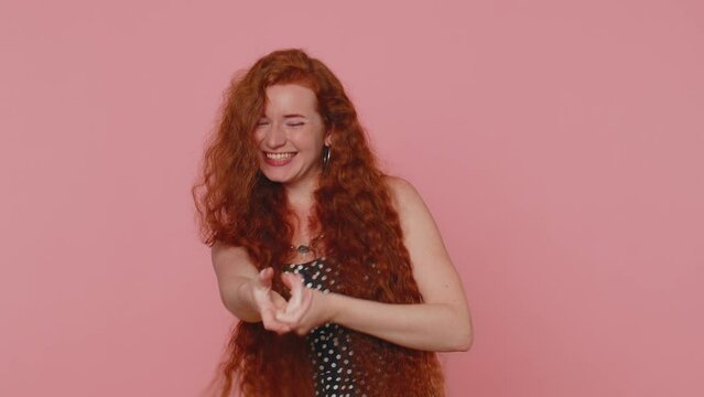Mime redhead woman in dress pulling an imaginary unreal invisible rope, puts lot of effort into showing how enduring, strong she is. Young ginger girl isolated alone on pink studio wall background