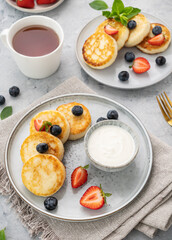 cheesecakes or  cottage cheese or syrniki with fresh blerries and sour cream on a gray background with a cup of tea. The concept of a healthy and delicious breakfast. Vertical orientation