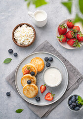Fototapeta na wymiar Cottage cheese pancakes with mint, blueberries and strawberries on a gray background. Healthy and delicious breakfast. Top view