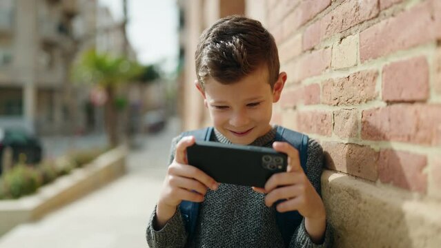 Blond child student watching video on smartphone standing at street