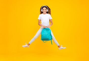 Fototapeta na wymiar Happy teenager portrait. Back to school. Schoolgirl student in headphones with school bag backpack on isolated studio background. School and education concept. Jump and run, jumping child.